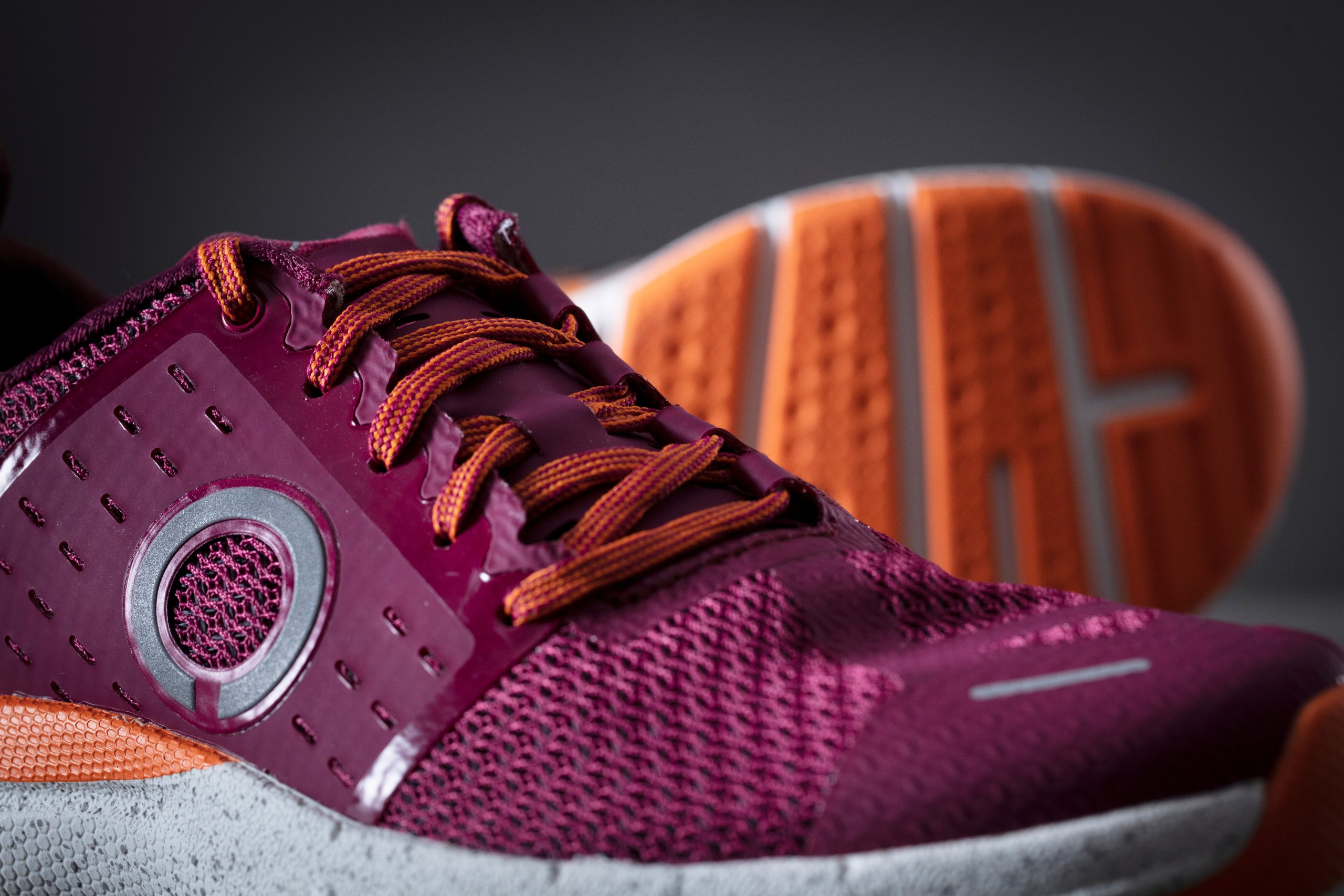 A close-up detail photo of a pair of running shoes. The shoes are magenta with copper and silver accents and copper-colored laces.